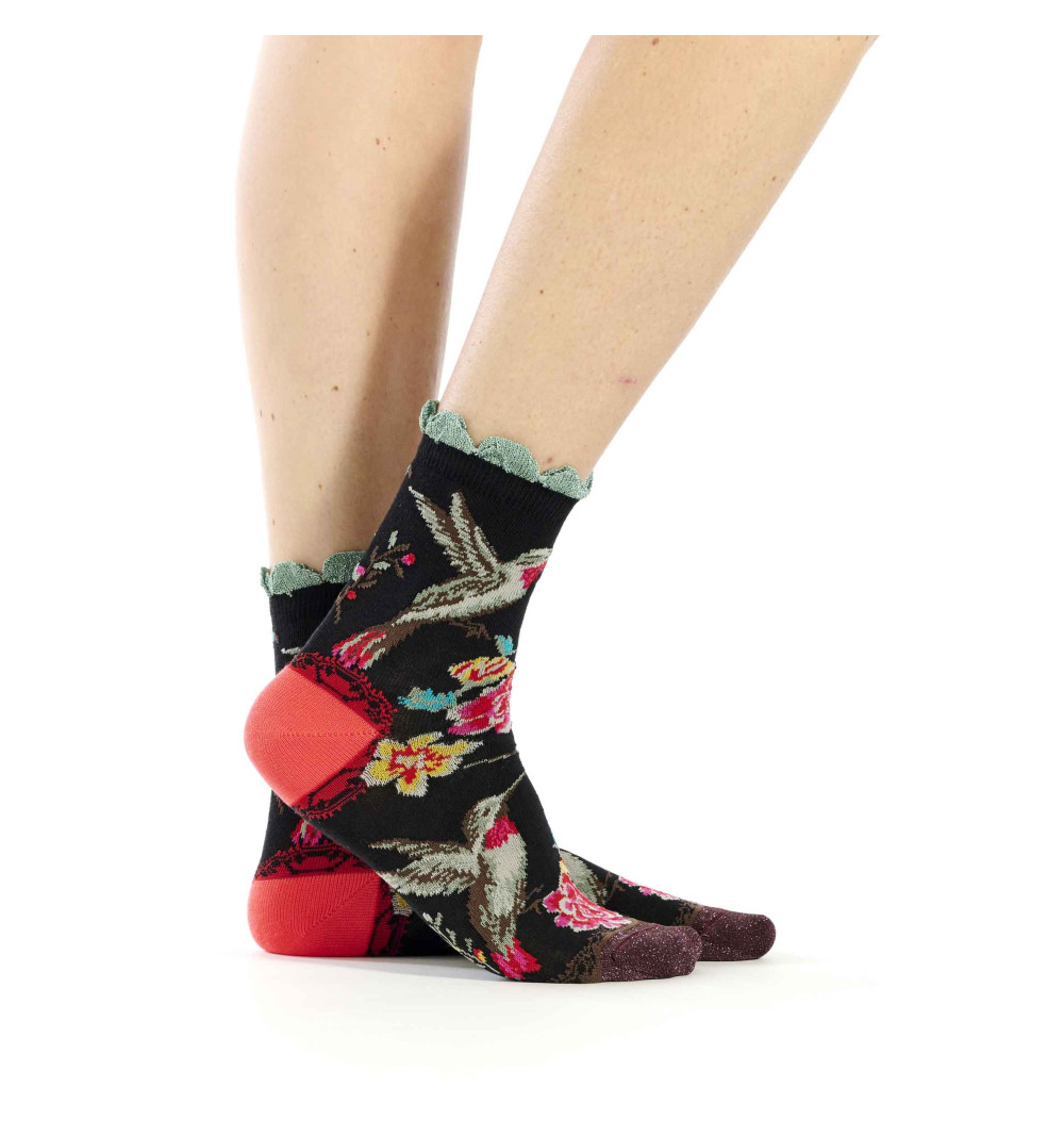 Chaussettes Dub & Drino noires ornées de colibris et de fleurs roses et jaunes. Talon rose et bord-côte festonné vert d’eau.